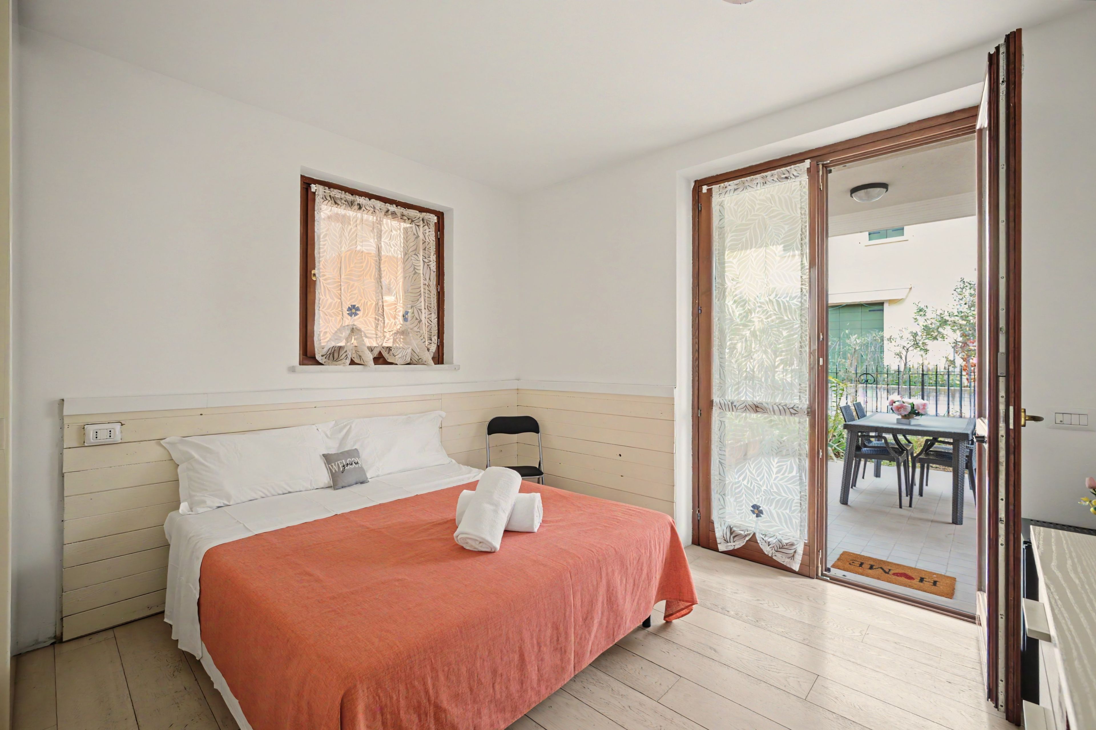 Een slaapkamer met een bed, een raam, een stoel en een schuifdeur naar een buitengebied.