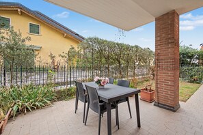 Une terrasse avec une table et des chaises, une colonne en briques et, au fond, un bâtiment jaune.