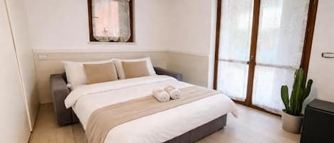 Un dormitorio con una cama, almohadas, una mesita de noche, una ventana con cortinas y una planta en maceta.