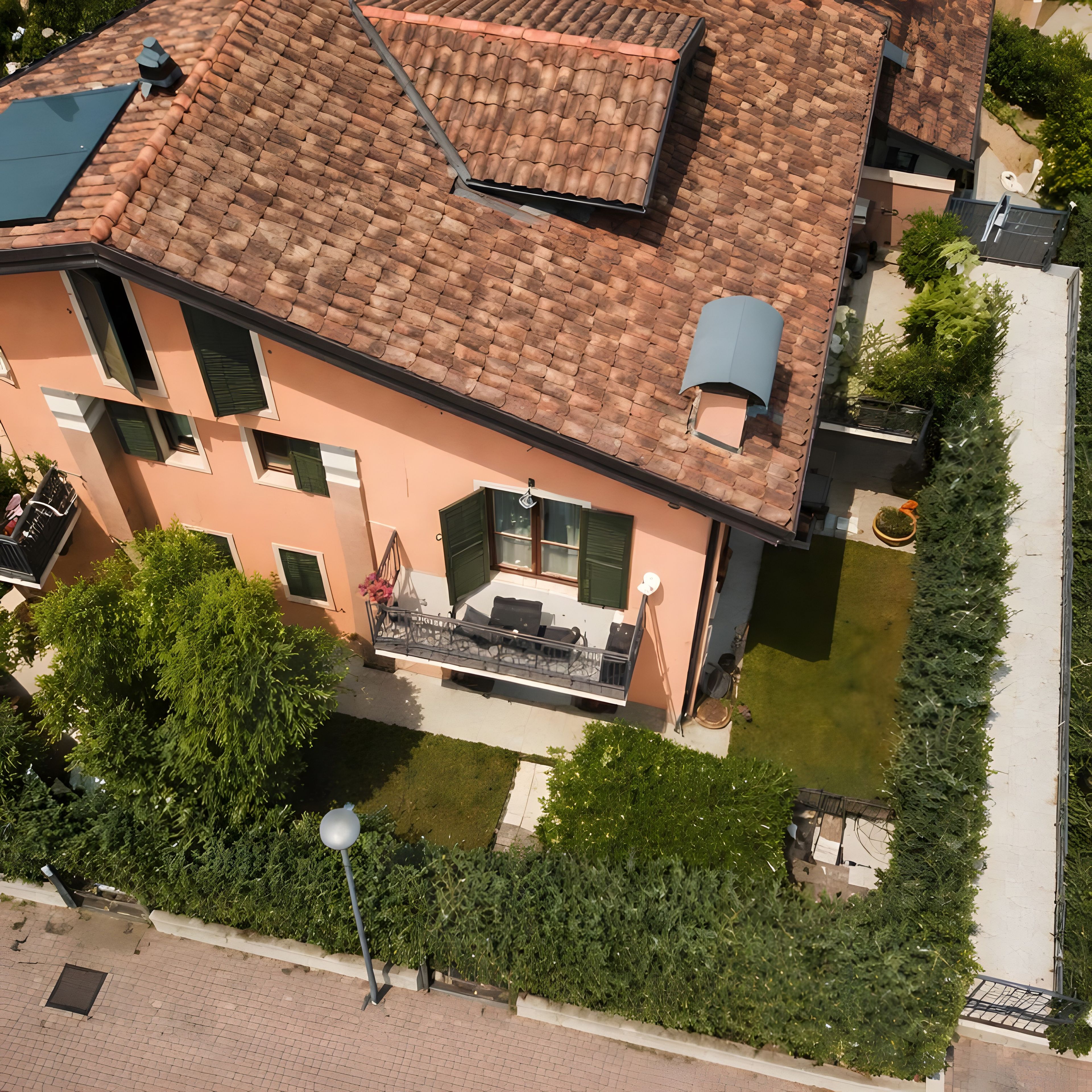 A multi-story building with a tiled roof, a balcony with outdoor furniture, and a well-maintained garden.