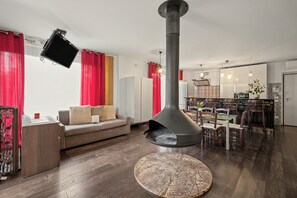 Un salon moderne avec une grande cheminée, un canapé, un coin repas et une cuisine en arrière-plan.