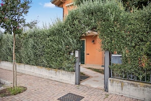 A paved pathway leading to a building with a green door, surrounded by dense foliage.