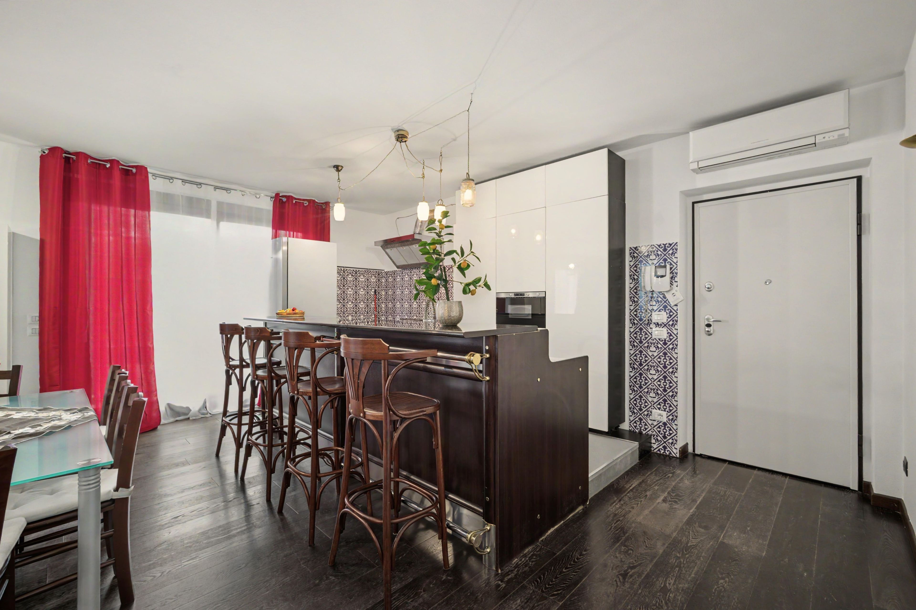 A compact kitchen with a central island, bar stools, a dining table, and a red curtain.
