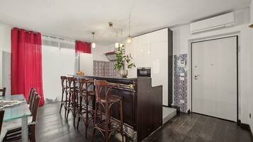 A compact kitchen with a central island, bar stools, a dining table, and a red curtain.