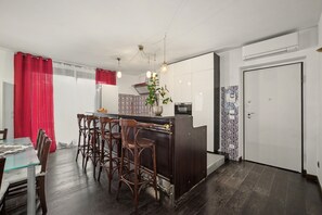 Cuina compacta amb una illa central, tamborets de bar, una taula de menjador i una cortina vermella.