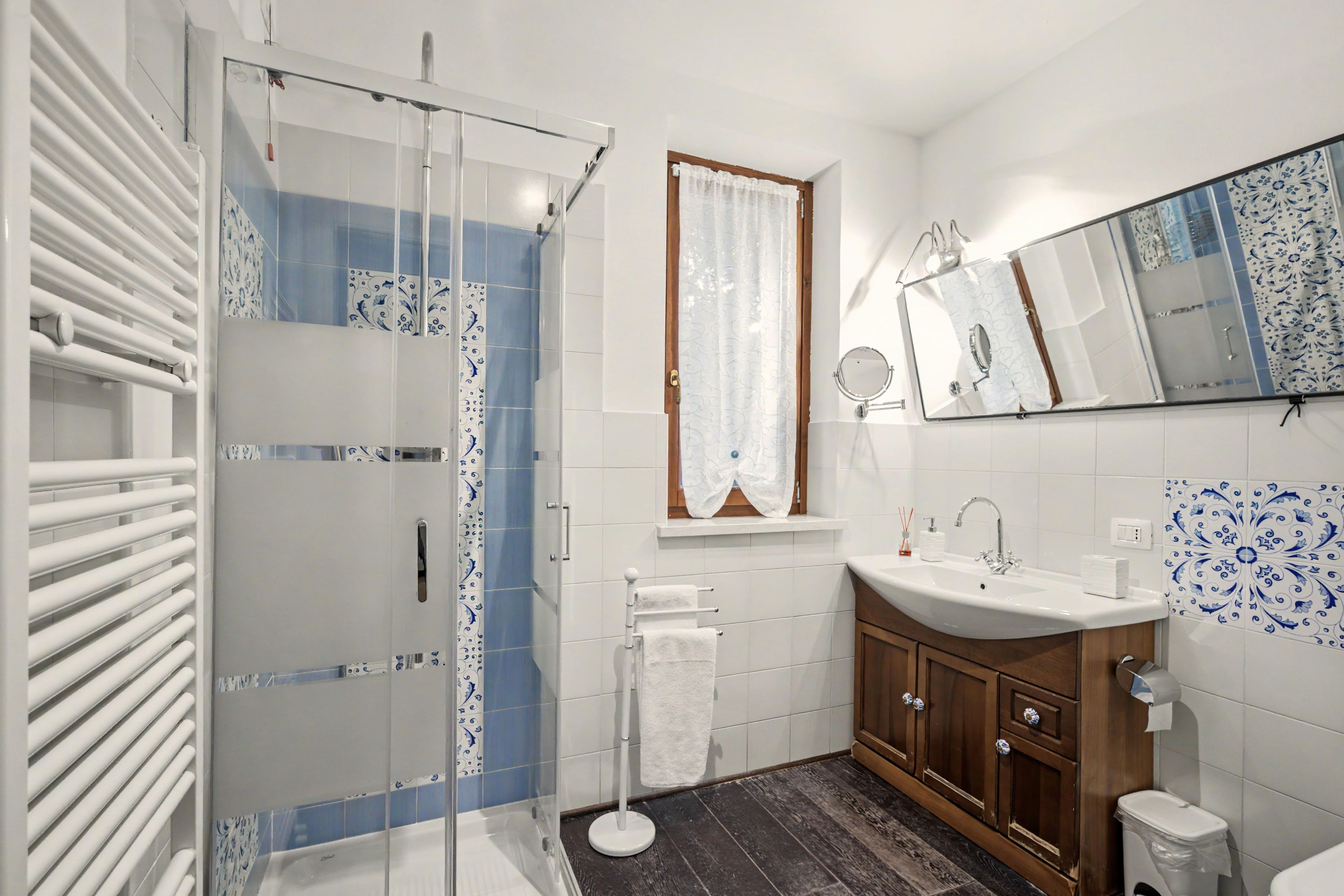 Un bagno moderno con box doccia in vetro, lavabo bianco con specchio sopra e piastrelle decorative alle pareti.
