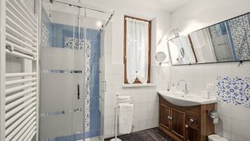 Un bagno moderno con box doccia in vetro, lavabo bianco con specchio sopra e piastrelle decorative alle pareti.
