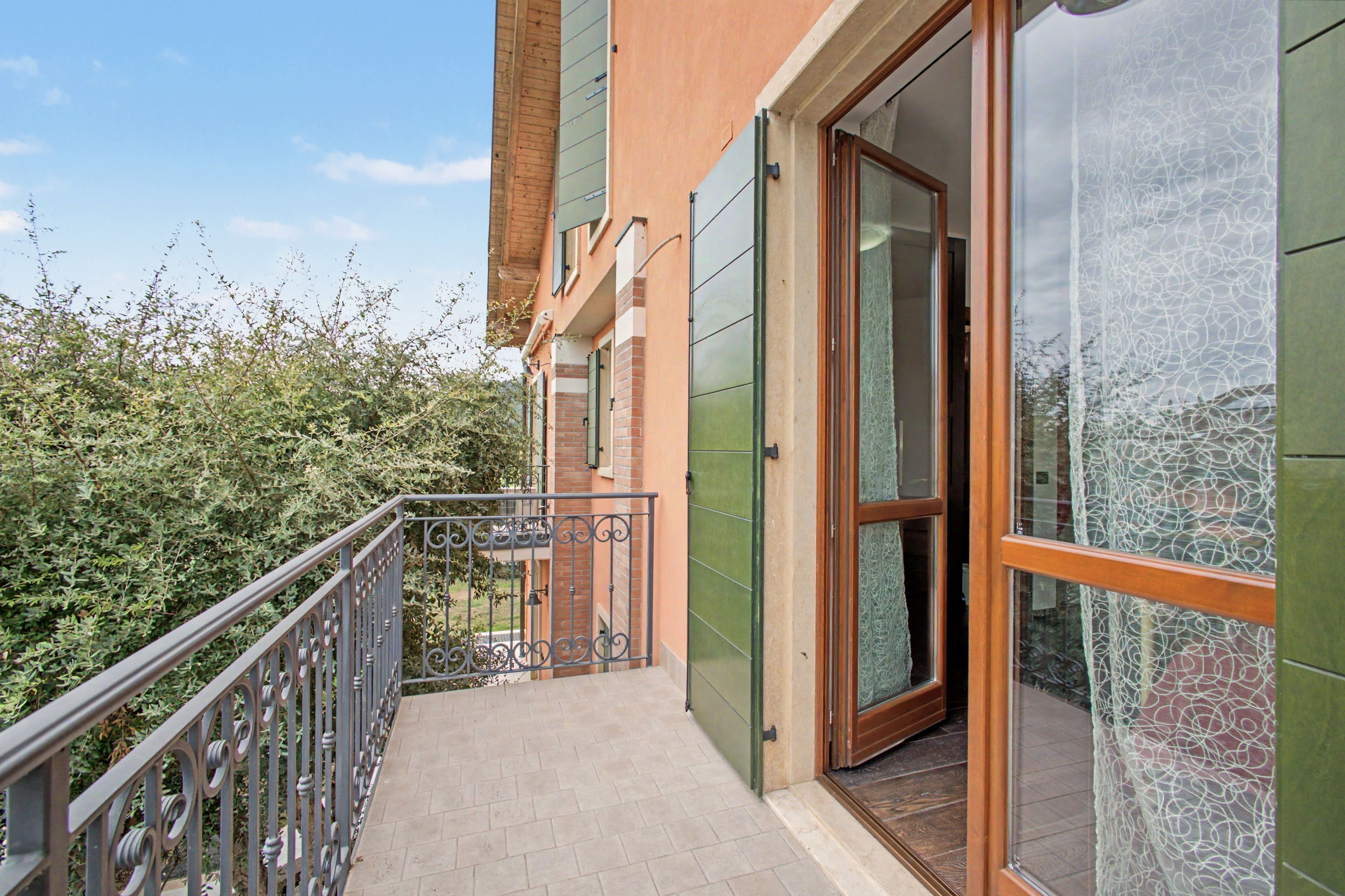 Ein Balkon mit Metallgeländer, eine Tür, die zu einem Innenraum führt, und Blick ins Grüne.