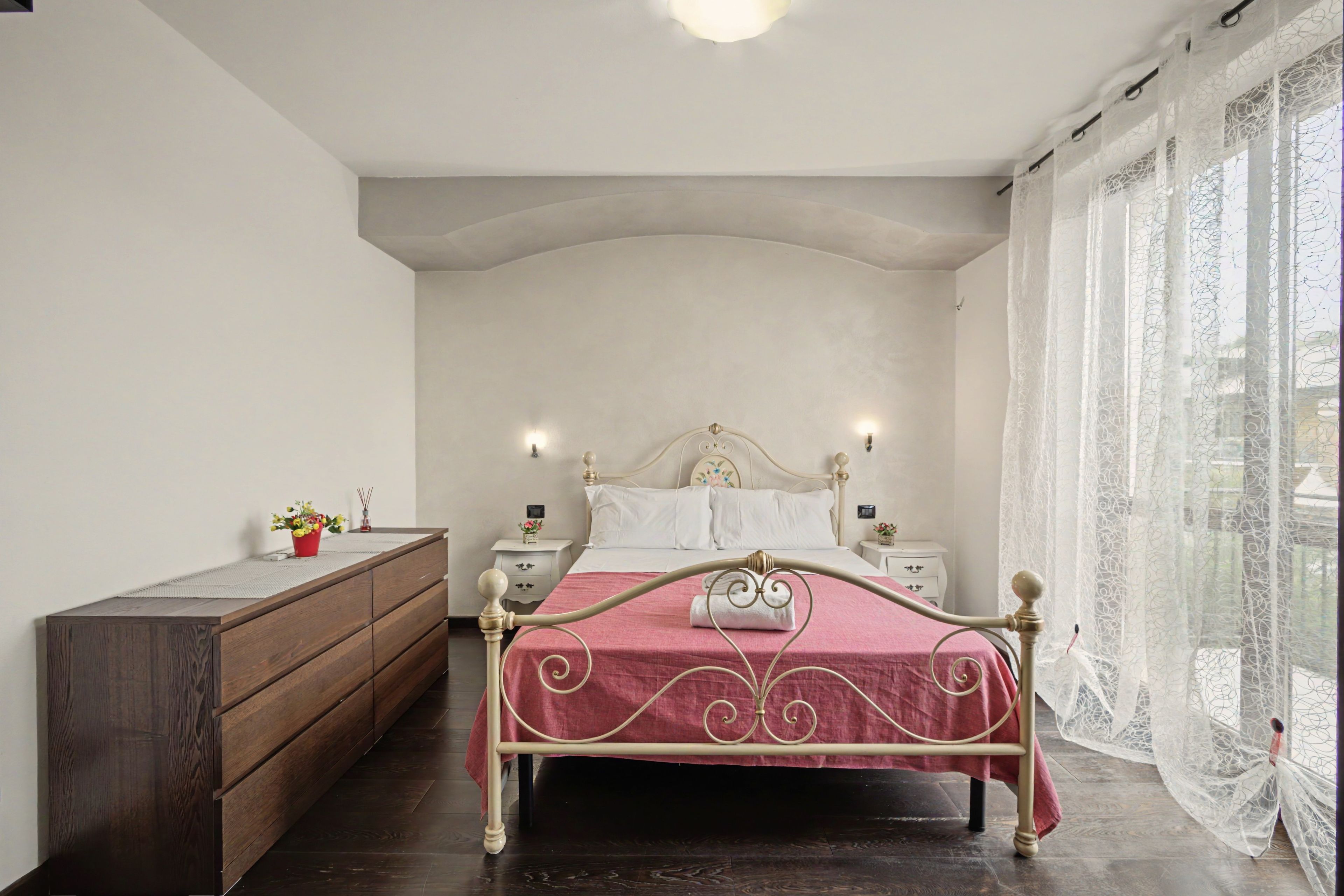 A bedroom with a bed, wooden dresser, nightstands, and a window with curtains.