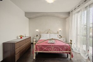A bedroom with a bed, wooden dresser, nightstands, and a window with curtains.