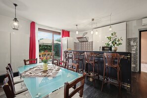 Una cuina moderna amb una illa central, una zona de menjador amb taula de vidre i vista a l'exterior.