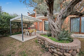 A patio area with a table and chairs under a canopy, surrounded by a stone wall and a large tree.
