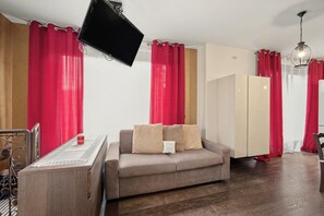 A room with a sofa, a television, a wardrobe, and a dining table.