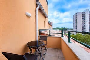 Un balcón con mesa y sillas, barandilla y vistas a edificios y árboles.