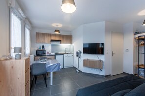 Ein kompakter Wohnbereich mit Küchenzeile, Essplatz, einer Couch und einem an der Wand befestigten Fernseher.