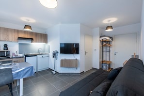 A modern living space with a kitchenette, a dining area, a sofa, and a TV mounted on the wall. - L’Escapade Marina - entre Camargue et Côte Bleue (Port-de-Bouc)