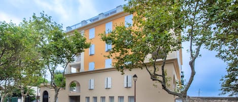 Ein mehrstöckiges Gebäude mit einer beigefarbenen Fassade und zahlreichen Fenstern, vor dem sich eine Straße erstreckt.