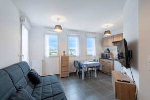 Un espacio habitable compacto con sofá, mesa de comedor, zona de cocina y vistas a través de las ventanas.