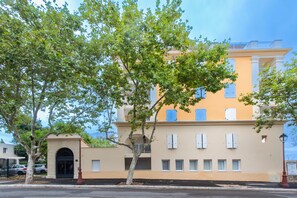 A two-story building with a beige facade, a black entrance door, and a balcony with blue shutters. - L’Escapade Marina - entre Camargue et Côte Bleue (Port-de-Bouc)
