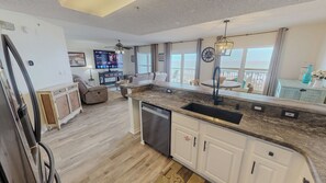 A modern kitchen with a built-in dishwasher, a large island with a sink, and a dining area with a view. - Spacious Beautiful Islander Beach 3009 (Fort Walton Beach)