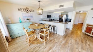 A modern kitchen with white cabinets, a central island, and a dining area with wooden chairs. - Spacious Beautiful Islander Beach 3009 (Fort Walton Beach)