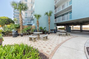 A courtyard with outdoor seating, palm trees, and a multi-story building with balconies. - Spacious Beautiful Islander Beach 3009 (Fort Walton Beach)