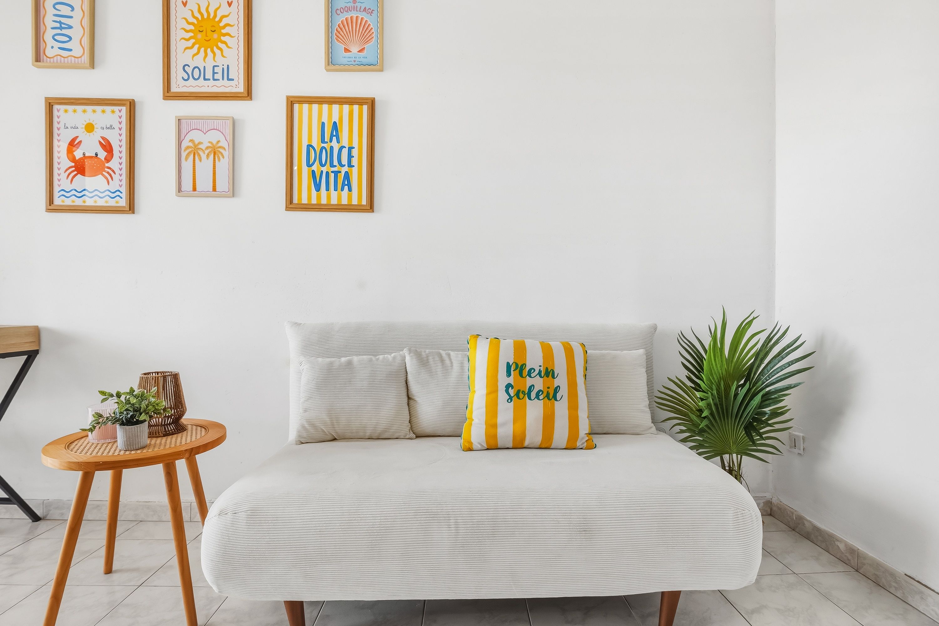 Ein Zimmer mit einer Couch, einem gestreiften Kissen, einem kleinen runden Tisch mit Pflanzen und Wandbildern in Rahmen.