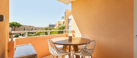 A balcony with a round table and chairs, a small cabinet, and a view of buildings in the background.