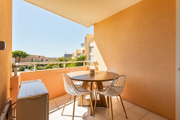 A balcony with a round table and chairs, a small cabinet, and a view of buildings in the background. - Le Petit Cocon de Sète - entre mer et lagune (Sète)