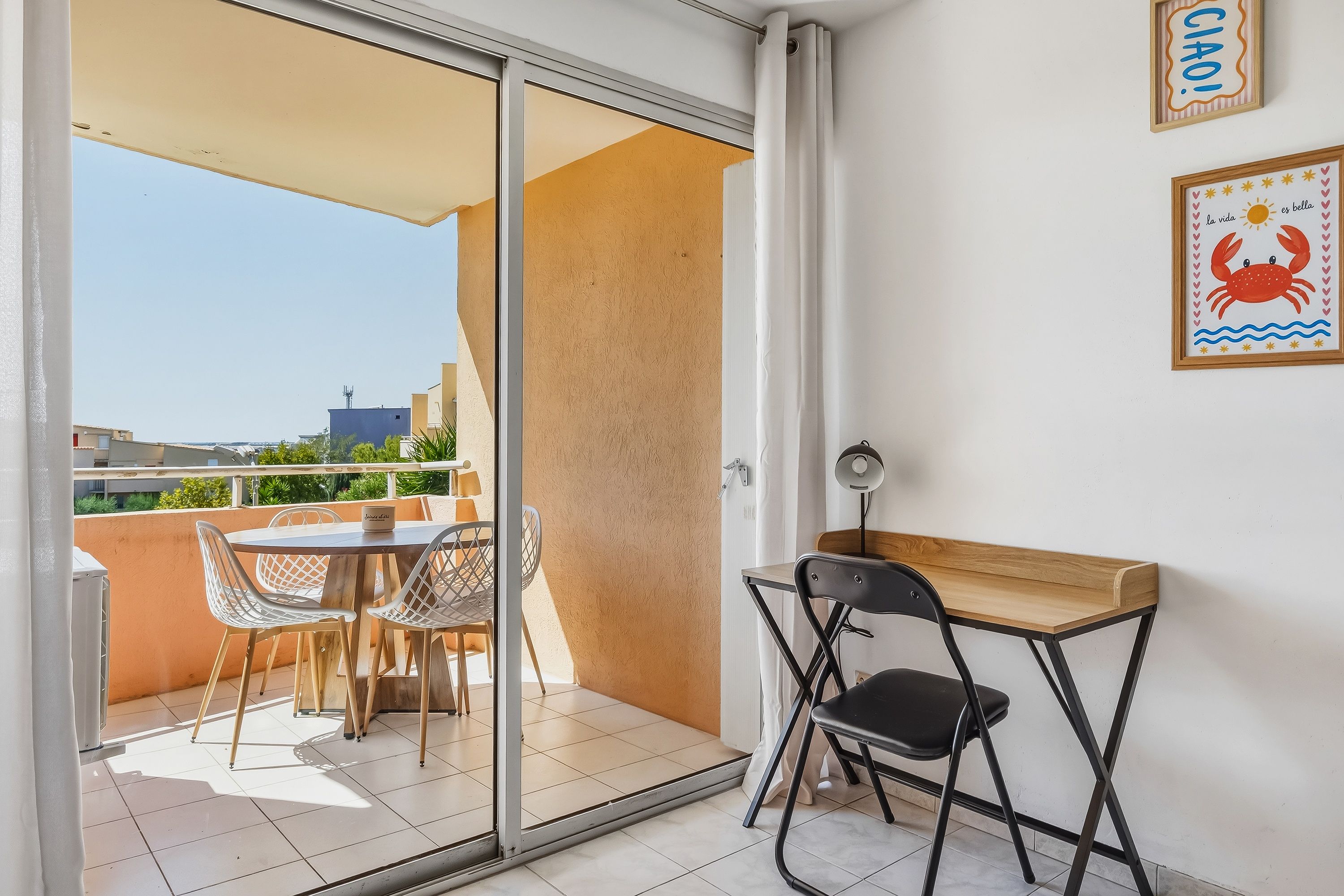A balcony with a table and chairs, a sliding glass door, and a wall with framed pictures.