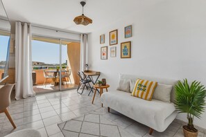 A modern living room with a sofa, a dining area with chairs, a table, and a balcony with a view. - Le Petit Cocon de Sète - entre mer et lagune (Sète)