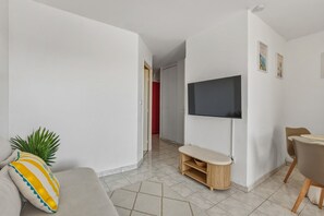 Ein modernes Wohnzimmer mit einem an der Wand befestigten Flachbildfernseher, einem Sofa mit einem gestreiften Kissen, einem kleinen Holztisch und einer Pflanze.