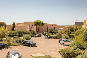 Ein Parkplatz mit mehreren Autos, umgeben von Grünflächen und Gebäuden im mediterranen Stil.