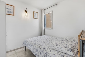 A bedroom with a bed, a wall-mounted light, a framed quote, and a window with curtains. - Le Petit Cocon de Sète - entre mer et lagune (Sète)