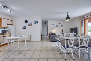 A modern kitchen with white cabinets, a dining table with chairs, and a living area with a sofa and a TV. - L’Escale du Teich - à 2 km de la gare (Le Teich)