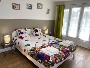 Uma cama com colcha florida, duas luminárias de cabeceira e uma janela com cortinas.