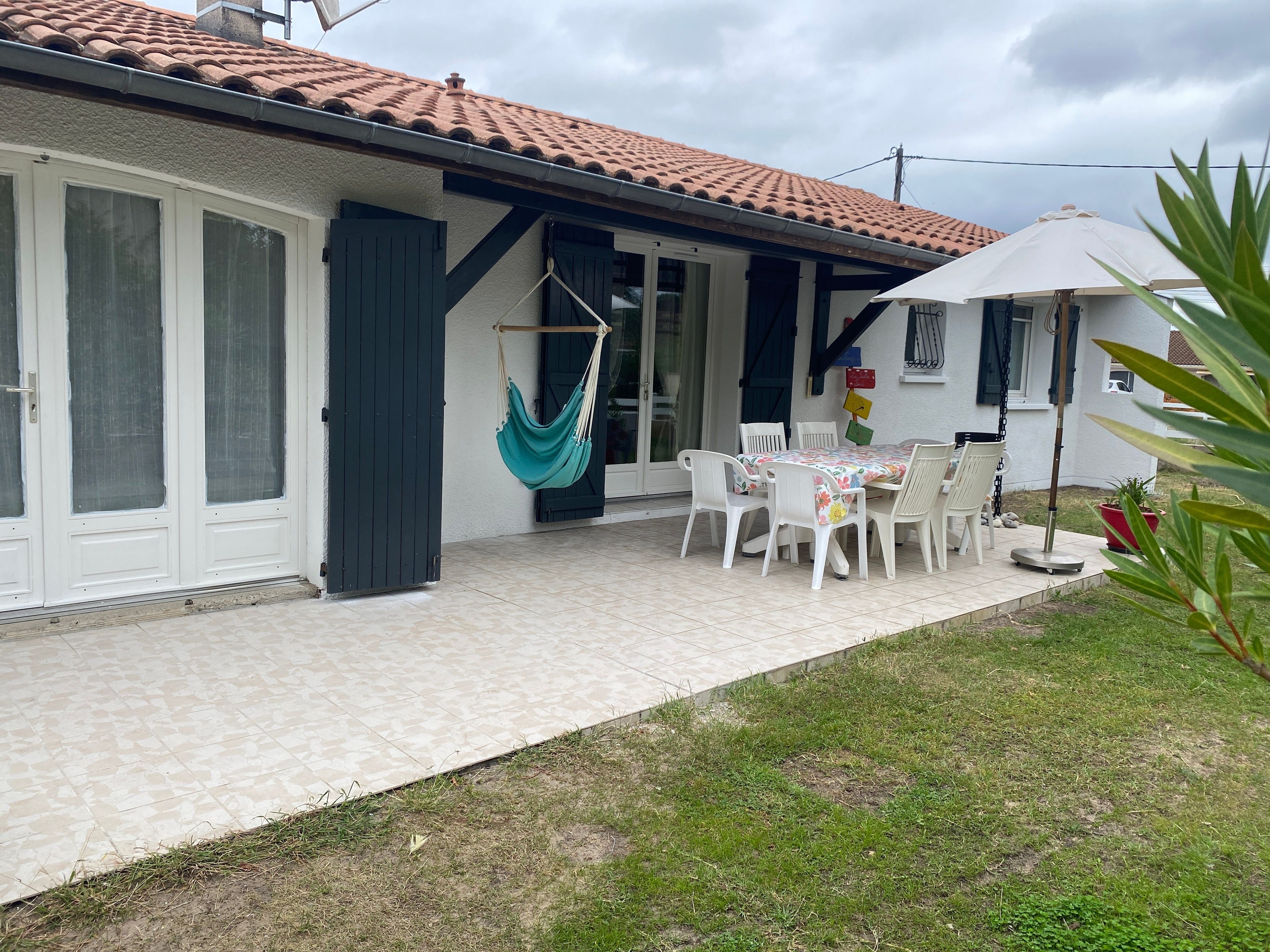 A house with a tiled roof, a covered patio with a table and chairs, and a hanging hammock.
