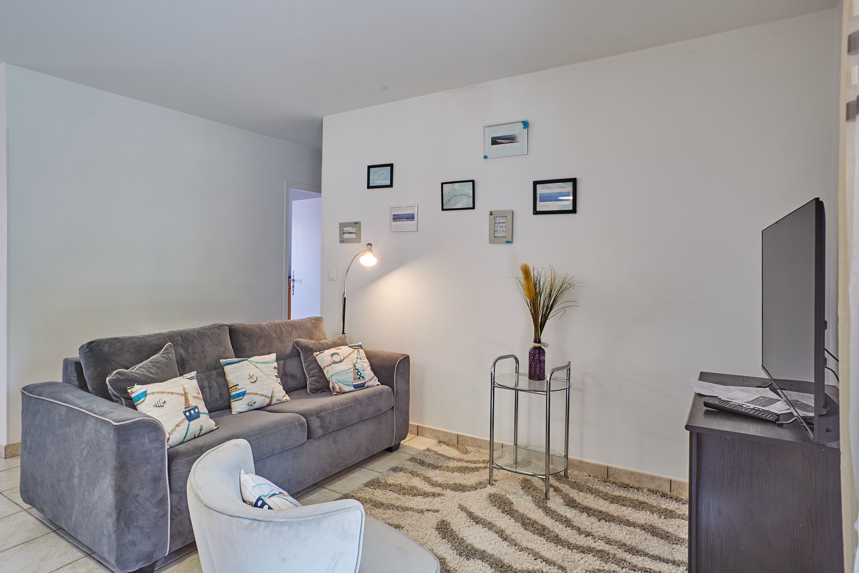 Ein modernes Wohnzimmer mit einem grauen Sofa, einem weißen Sessel, einem Glastisch und einem Flachbildfernseher.