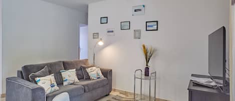 Ein modernes Wohnzimmer mit einem grauen Sofa, einem weißen Sessel, einem Glastisch und einem Flachbildfernseher.
