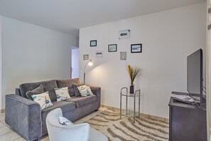 Uma sala de estar moderna com um sofá cinzento, uma poltrona branca, uma mesa de centro de vidro e uma televisão de tela plana.