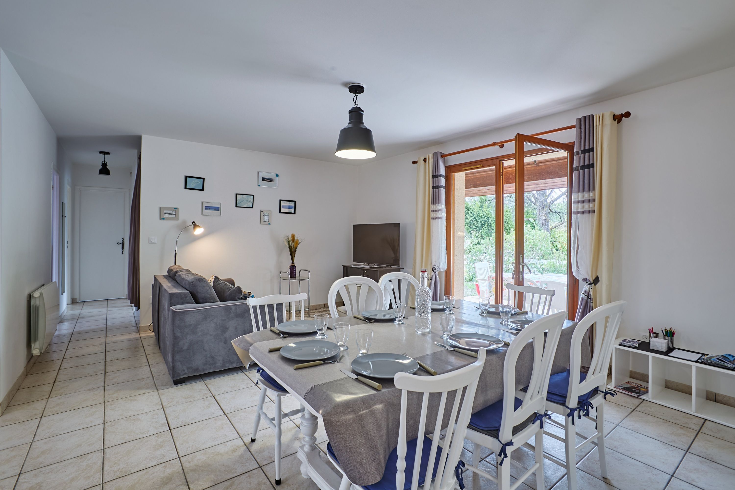 A modern living room with a dining area, white furniture, a flat-screen TV, and framed pictures on the wall.