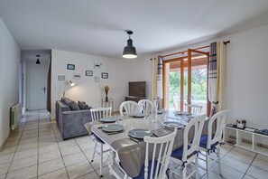 Uma sala de estar moderna com área de jantar, mobiliário branco, TV de tela plana e quadros nas paredes.