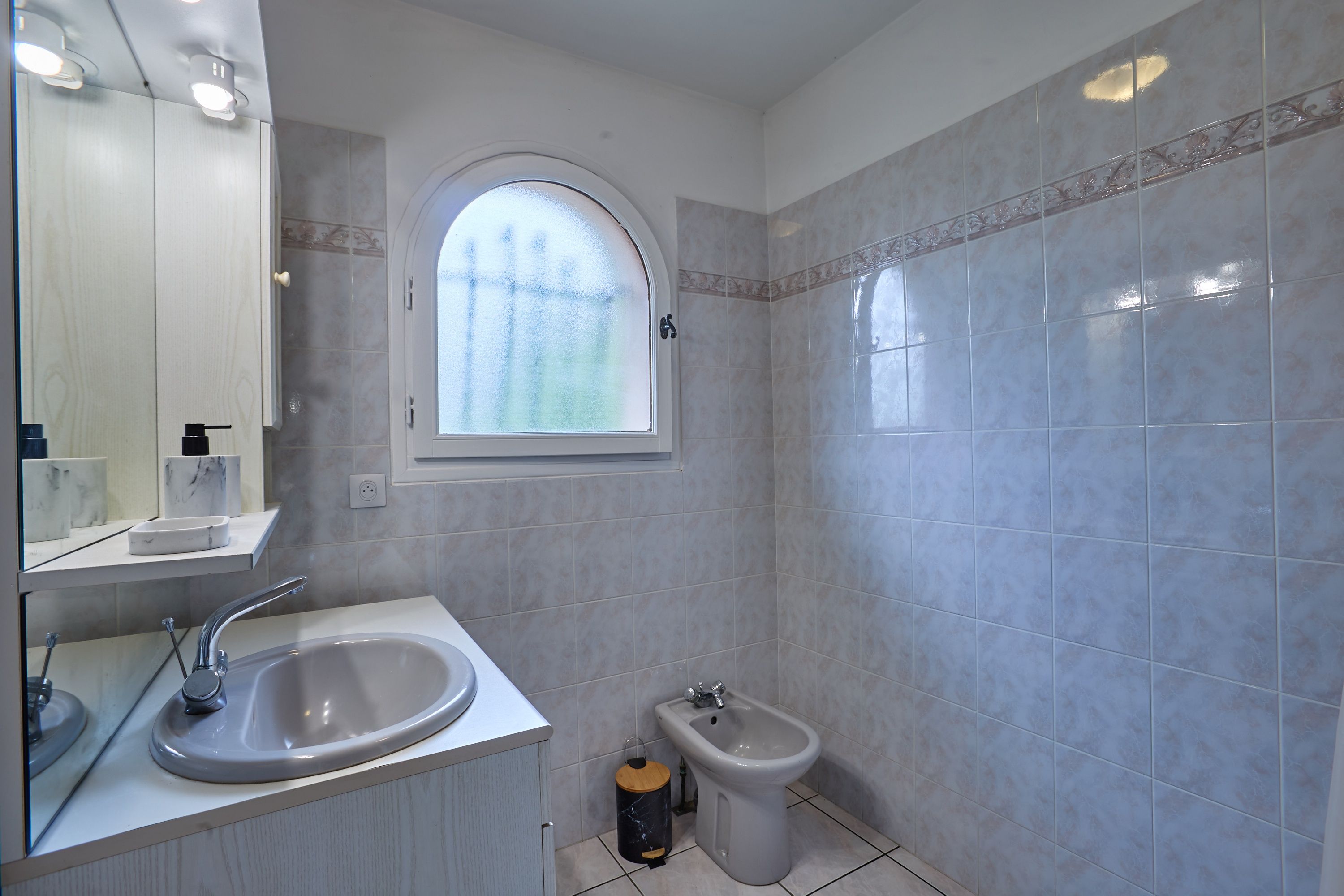 A bathroom with a large mirror, a sink, a bidet, and a window.