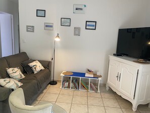 A living room with a sofa, a television, a floor lamp, a bookshelf, and a cabinet. - L’Escale du Teich - à 2 km de la gare (Le Teich)