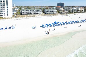A beach with rows of blue umbrellas and lounge chairs, a clear shoreline, and buildings in the background. - Beautiful Spacious Townhome SBAY 54 (Destin)