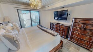 A hotel room with a large bed, a wooden dresser, a television mounted on the wall, and a balcony with a view of buildings. - Stunning Inlet Reef 615 w/private top floor balcony (Destin)