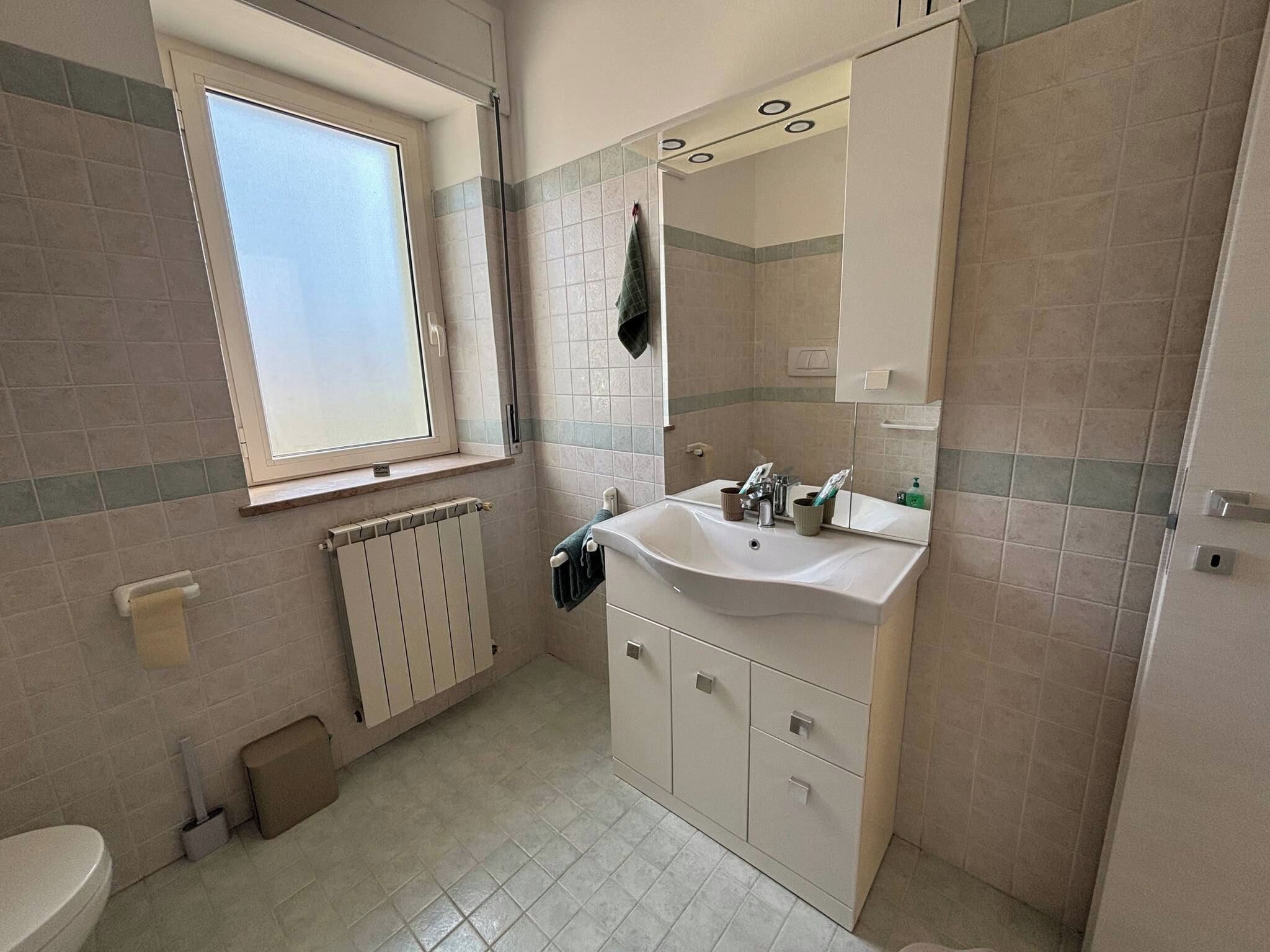 A bathroom with a window, a sink, a mirror, and a toilet.