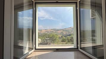A room with a large window offering a view of a hilly landscape.