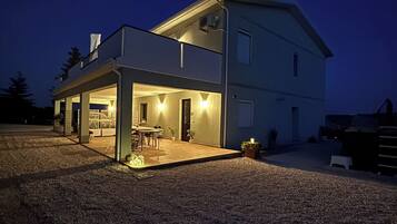 Ein zweistöckiges Haus mit einer überdachten Terrasse und einem kleinen Garten.