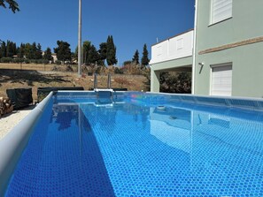 Una piscina con superficie azul cristalina, rodeada por una valla y árboles.